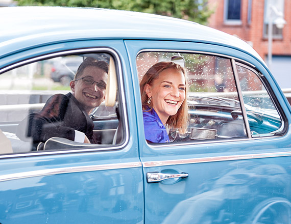 Lachendes Brautpaar im taubenblauen VW Käfer Hochzeitsauto